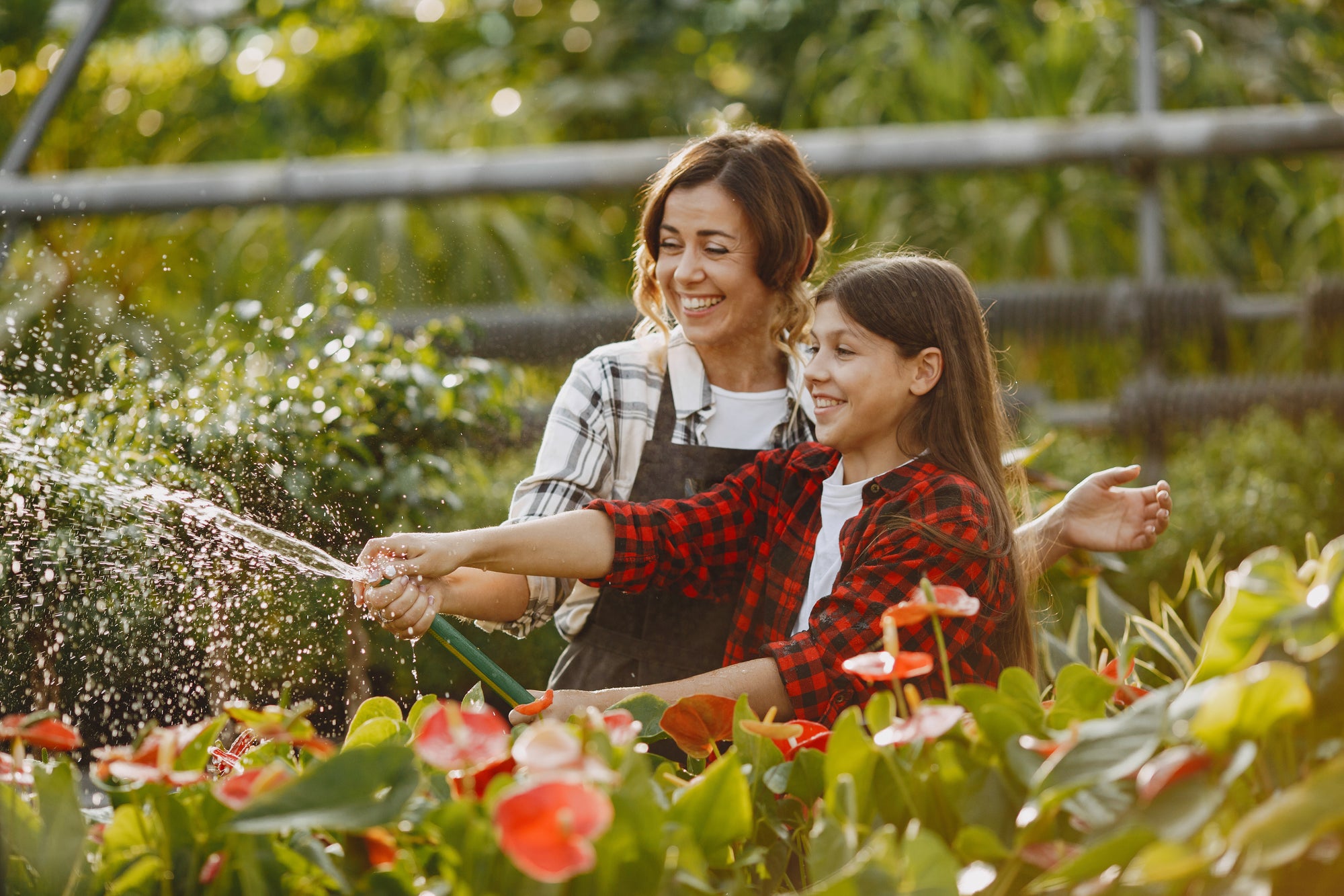 Woman and child in a garden, with the woman watering plants and the child looking on.